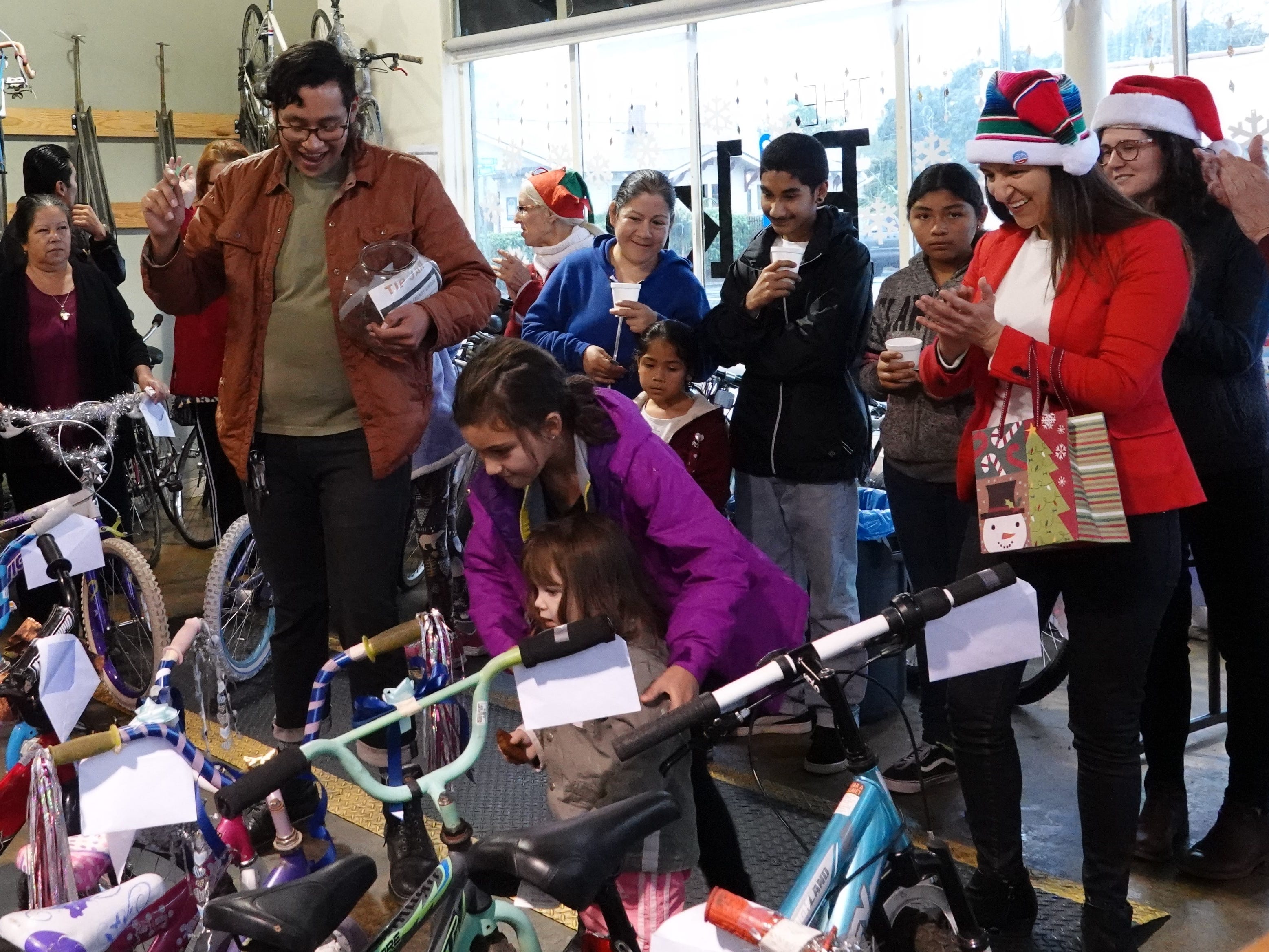 Jazzlyn Gerardi, in purple coat, helps her 2-year-old sister Brighton retrieve the bicycle she got Sunday during a holiday bike giveaway at Ventura Bike HUB. At left, staff member Alex Penaloza holds up the winning raffle ticket while Ventura Deputy Mayor Sofia Rubalcava, at right in striped hat, looks on.