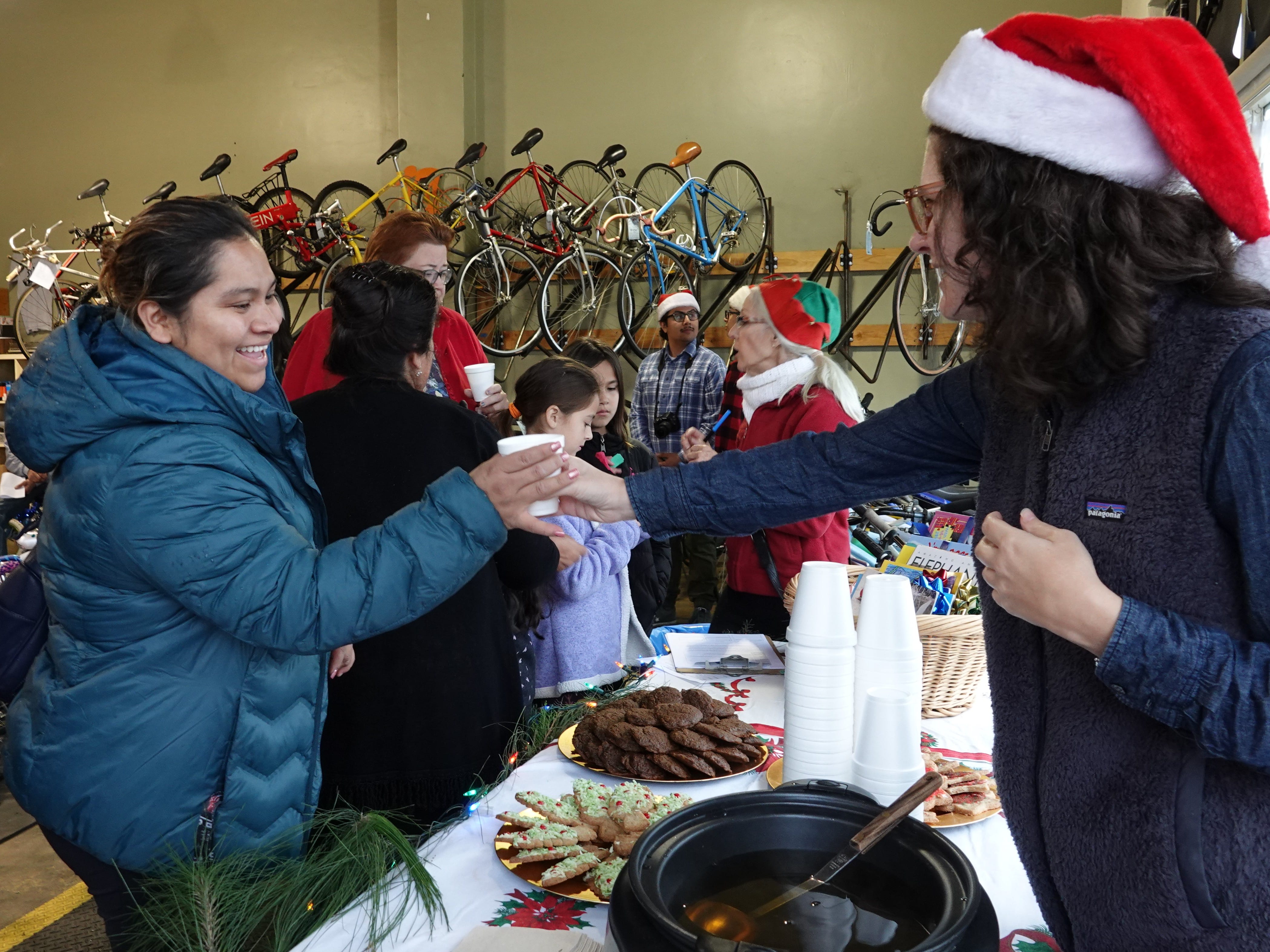 Volunteer Lauren Steinbaum, right, handed out cider and cookies to families attending the holiday bike giveaway at Ventura Bike HUB on Sunday.