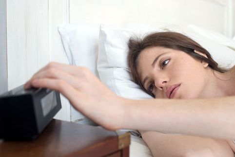 Woman in bed pressing alarm clock snooze button