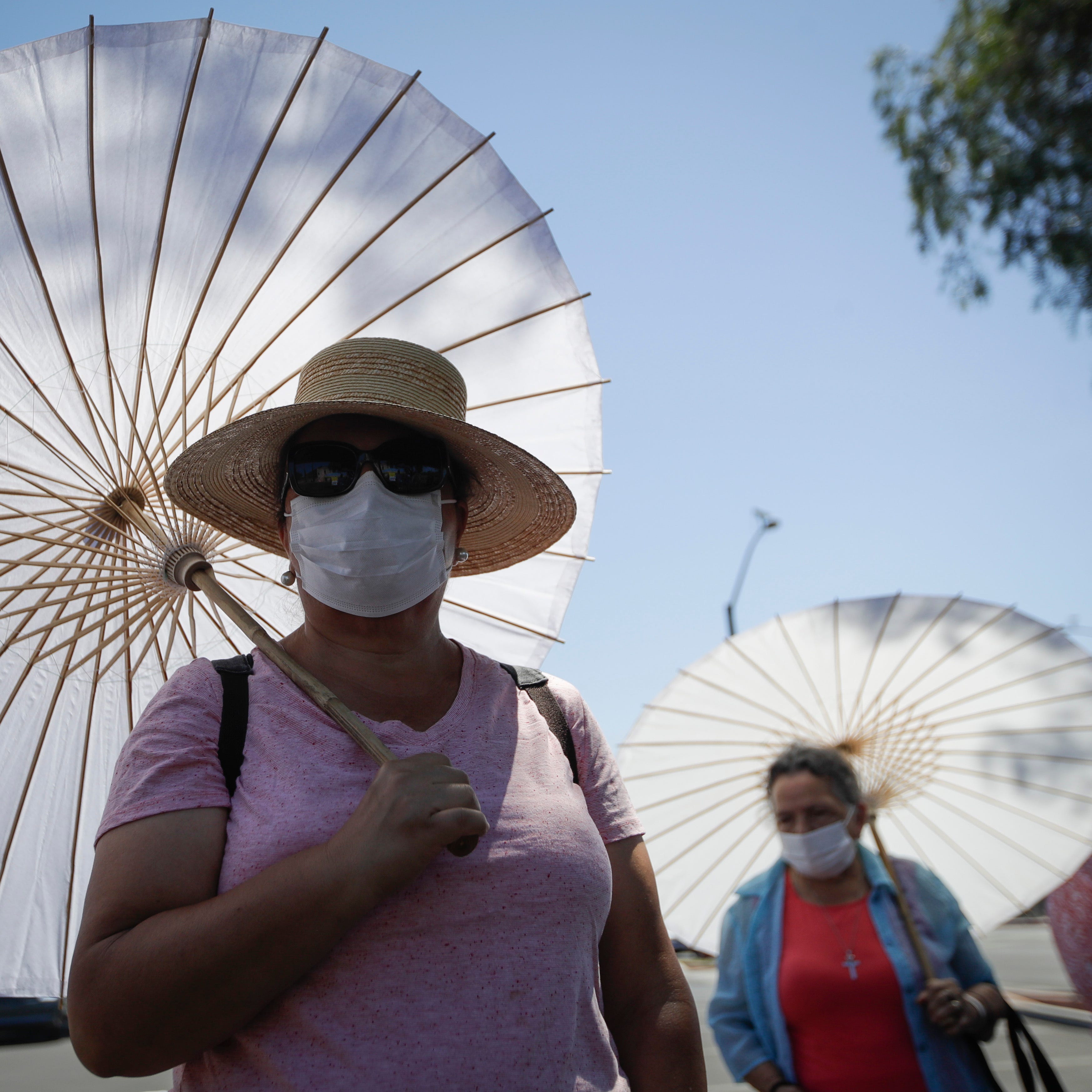 The faithful use face masks and parasols during an outdoor prayer amid the coronavirus pandemic at the San Gabriel Mission, Sunday, July 12, 2020, in San Gabriel, Calif.