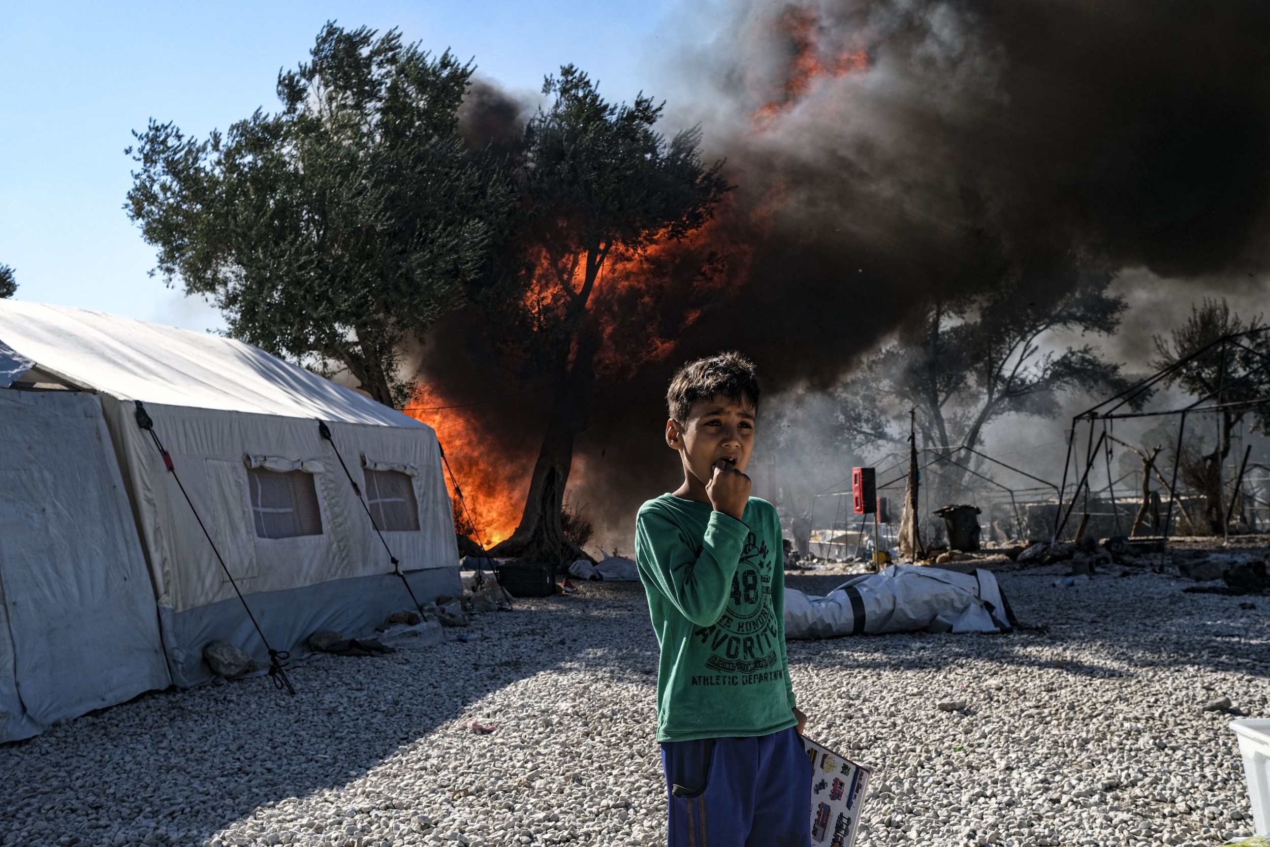 A distressed boy stands in front of a fire which destroyed Moria camp in Lesbos.